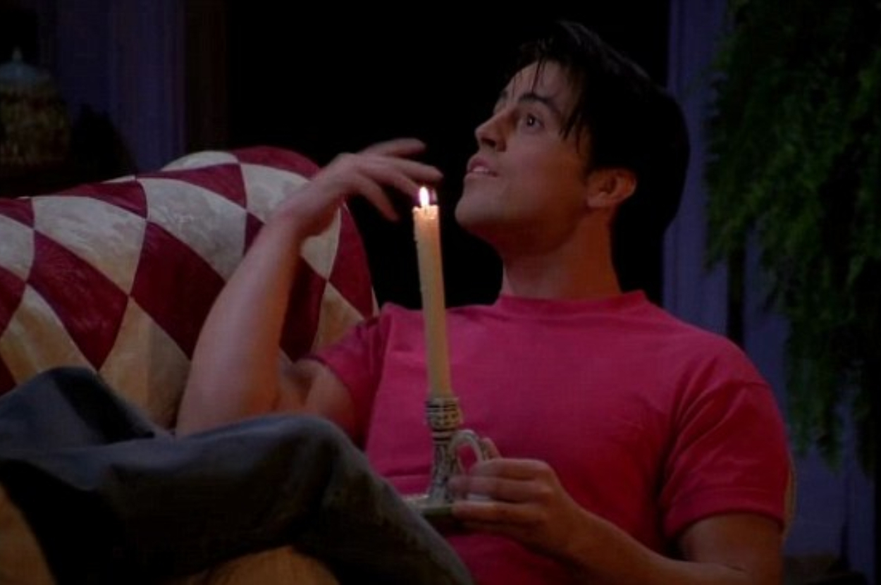 Person in pink shirt lying down, looking at a lit candle, expressing wonder