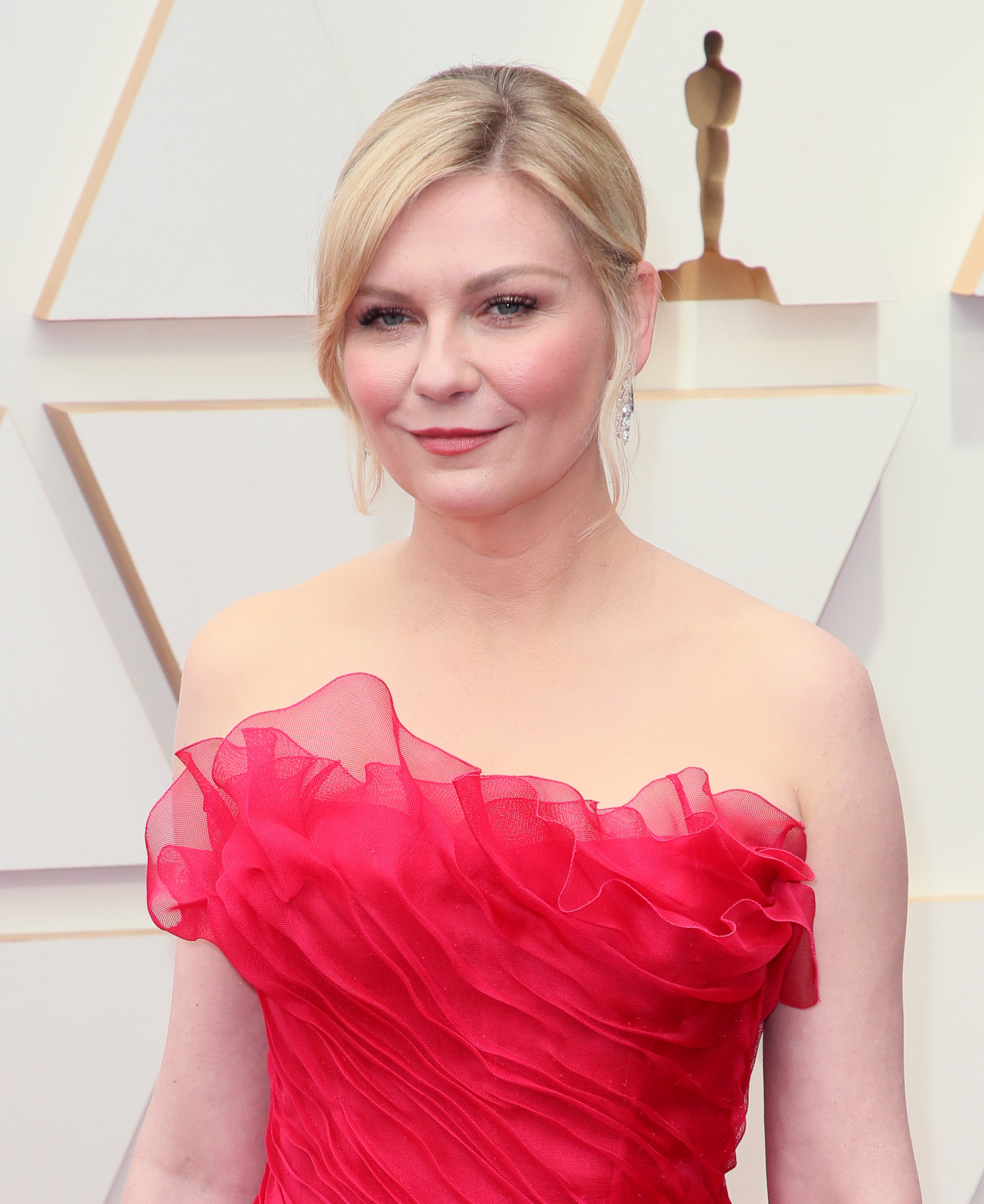 Kirsten in an elegant strapless ruffled gown posing for a photo on the Oscars red carpet