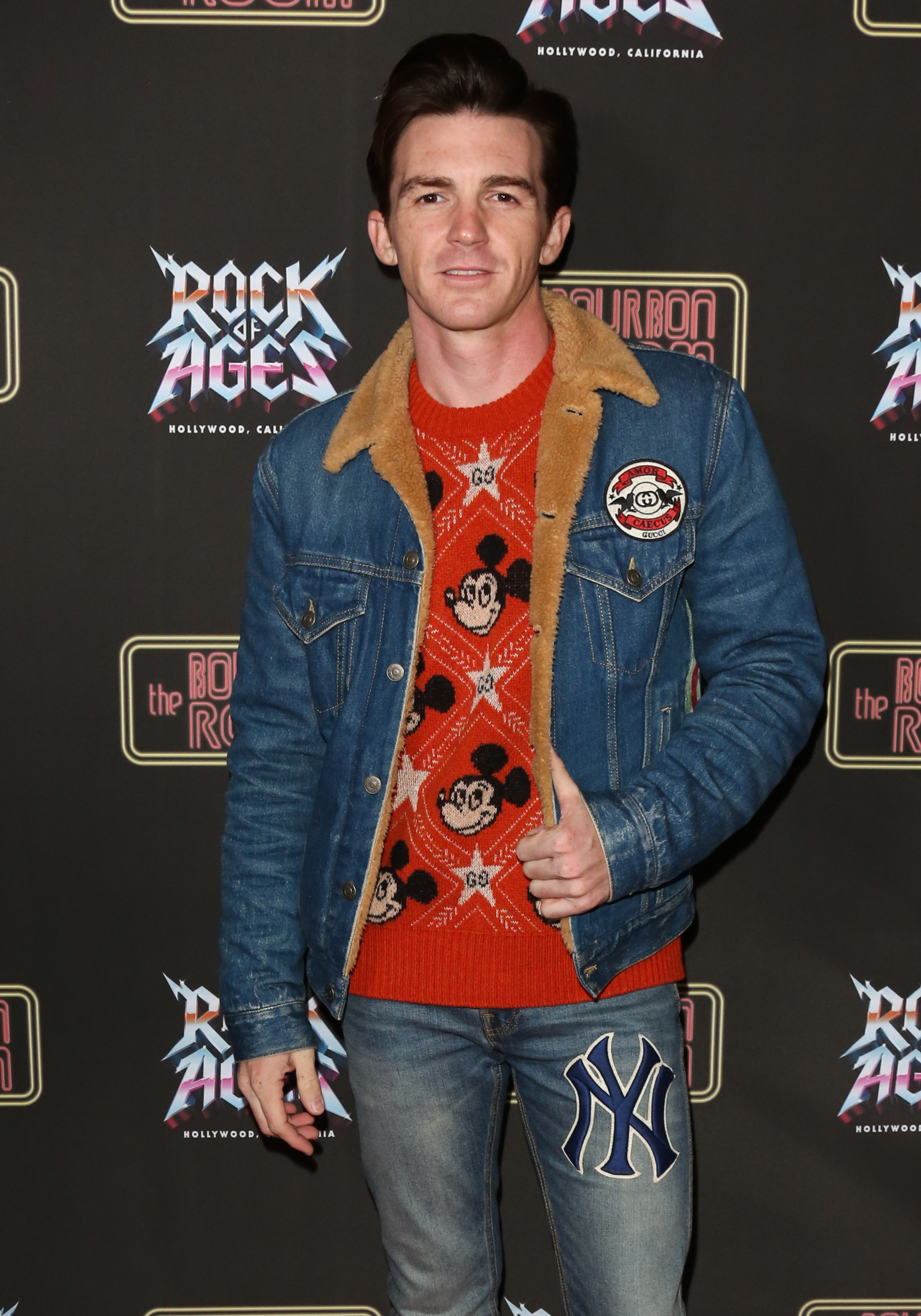 Drake Bell at an event wearing a denim jacket, patterned sweater, and jeans