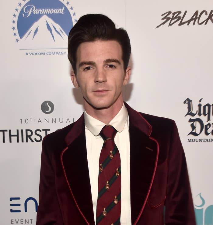 Drake Bell in a velvet suit with a patterned tie, posing for photographers at a red carpet event