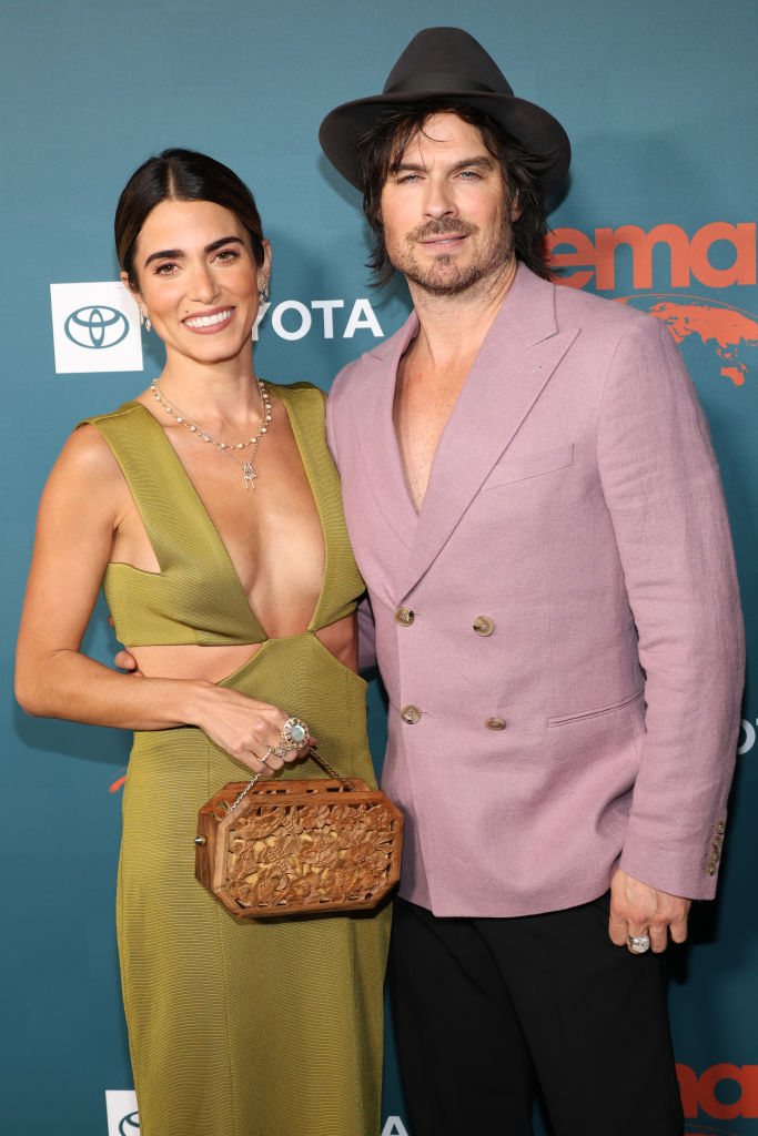 the couple posing together, Nikki in a sleeveless dress with a carved clutch, Ian in a double breasted suit and fedora