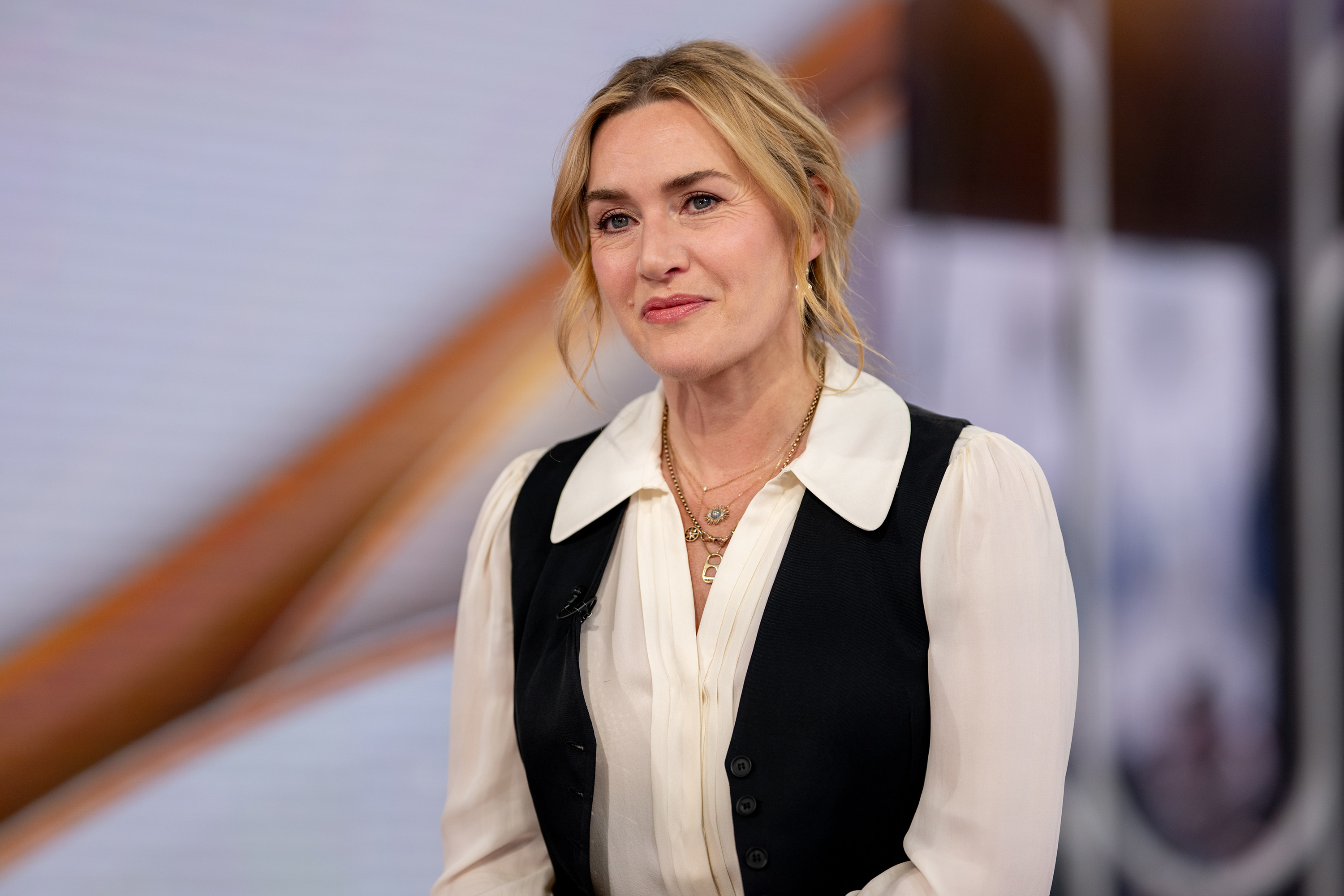 Kate Winslet in a vest and long-sleeved blouse smiles during an interview