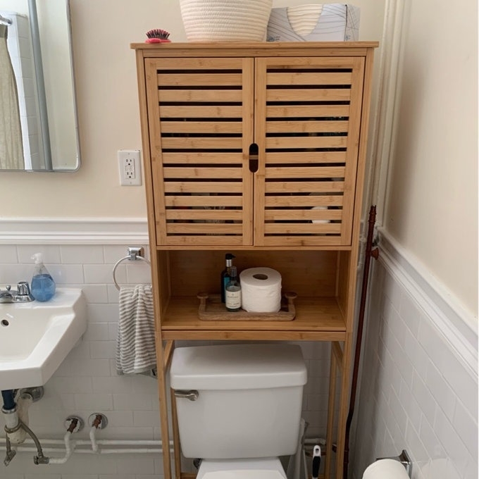 reviewer image of a wooden bathroom cabinet over a toilet with closed upper doors and open shelf with toiletries