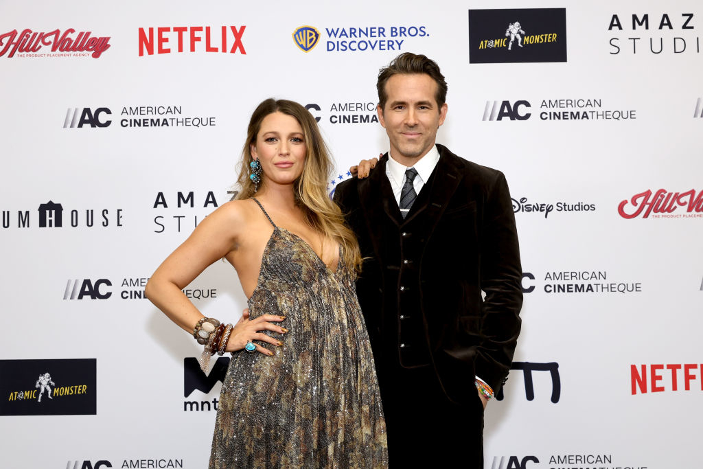 Blake Lively and Ryan Reynolds smiling, standing close, Lively in a patterned dress and Reynolds in a suit