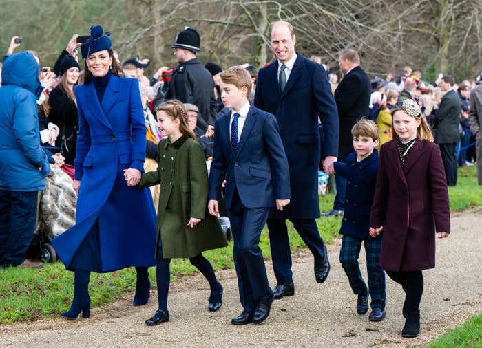 William and Kate with their children walking outside, dressed in winter coats as onlookers stand on the side