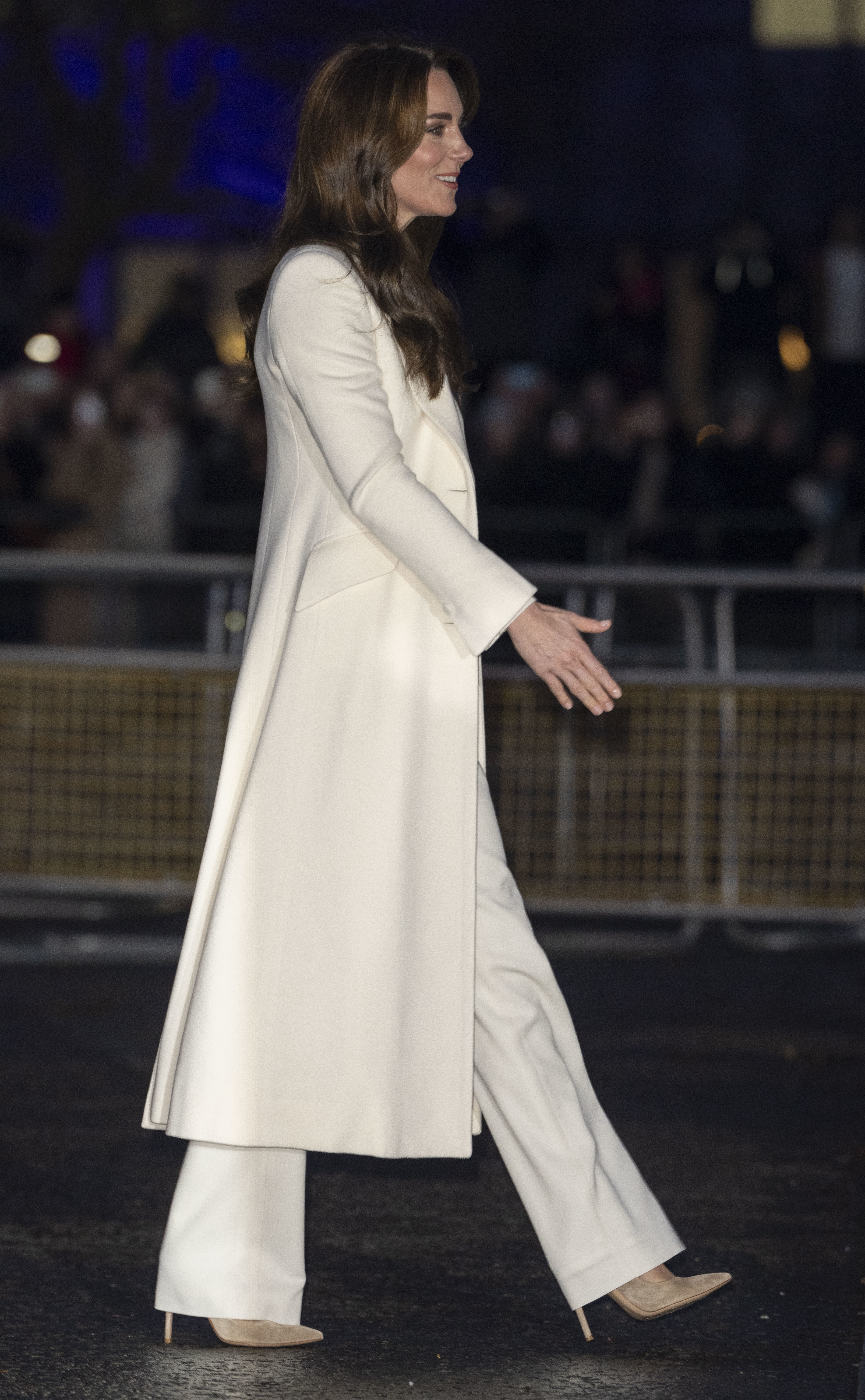 Kate Middleton in a long coat and trousers walking outside at night