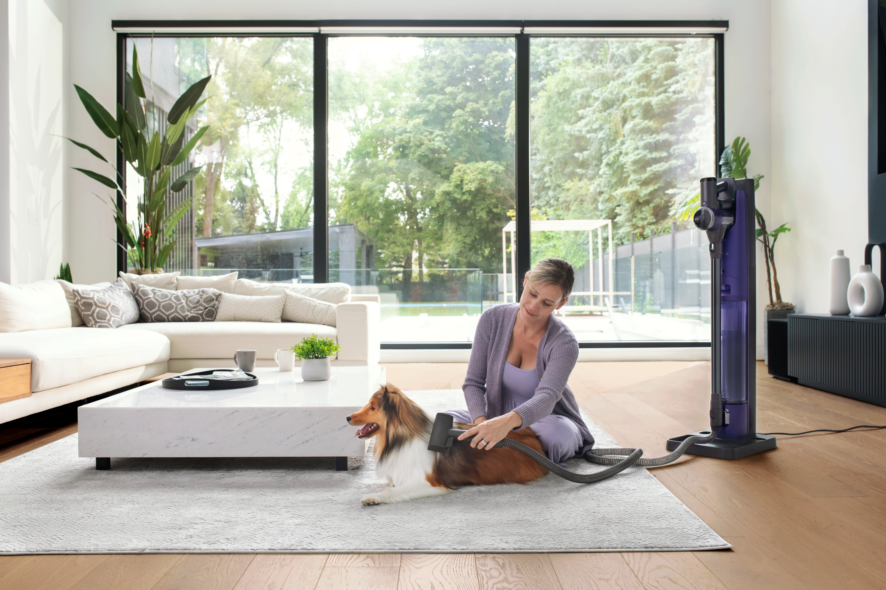 Woman sitting with dog beside a vacuum cleaner in a modern living room