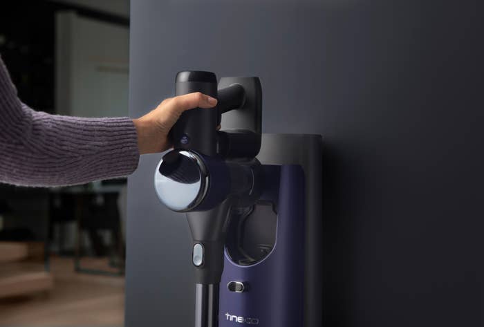 Hand placing a cordless vacuum onto a wall-mounted charging dock