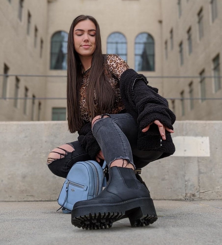Person in ripped jeans and chunky boots sitting on a step, with a leopard print top and black outerwear