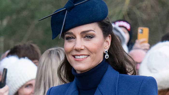 Kate in a hat and navy coat at a public event, smiling