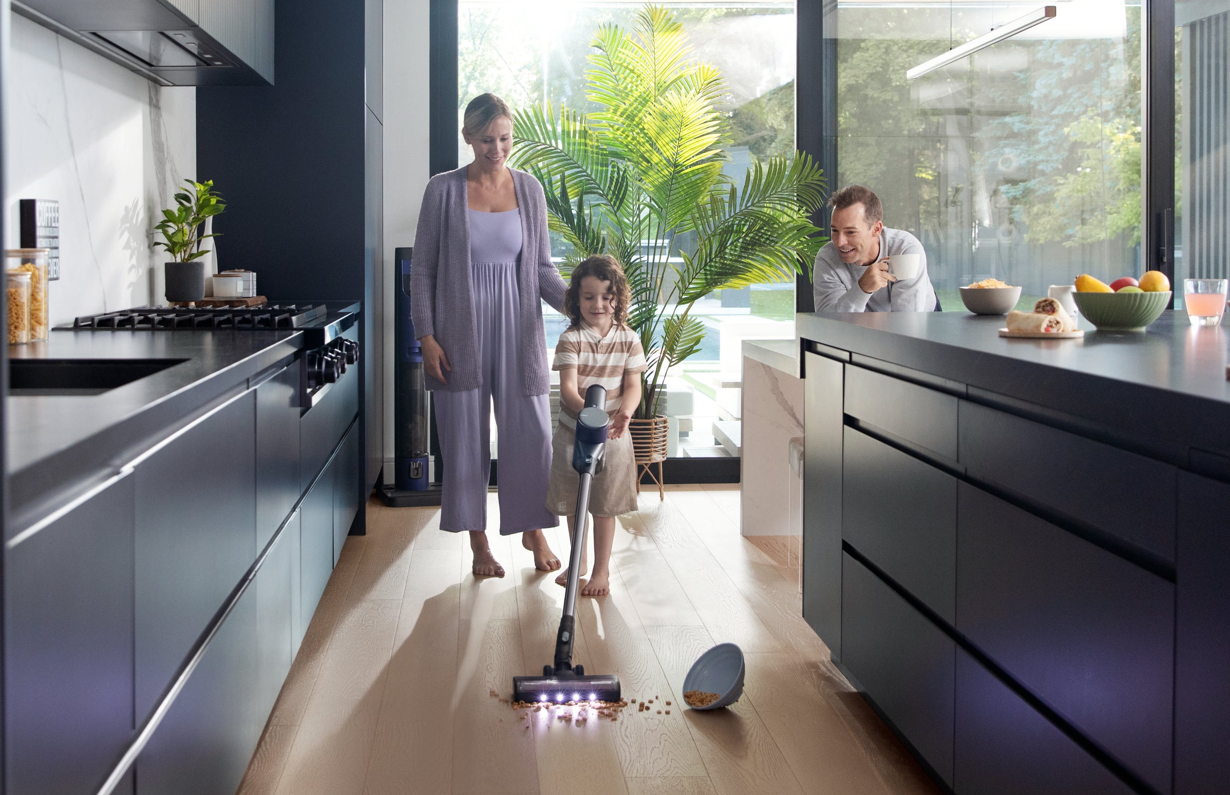 Family interacts in a modern kitchen with a child playing on the floor and two adults supervising