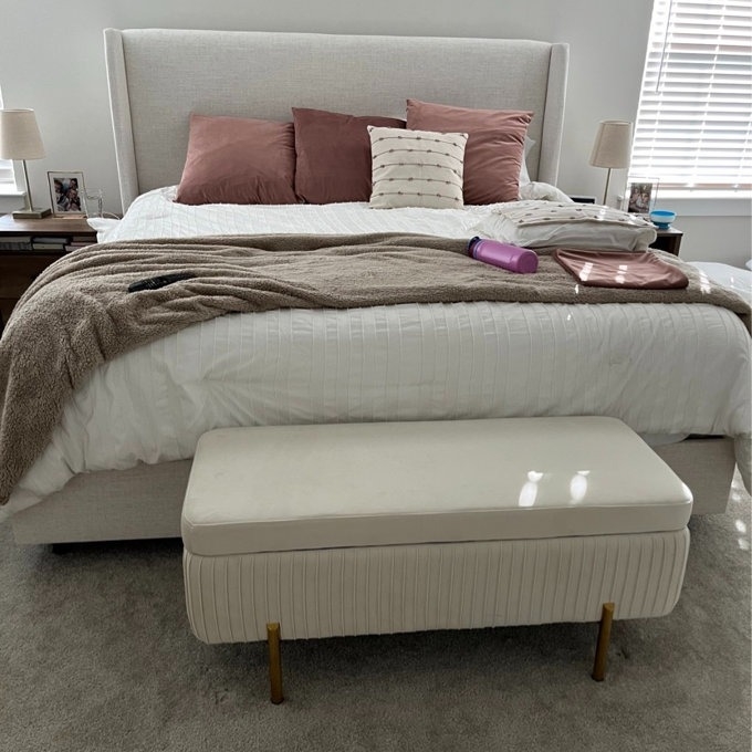 A neatly made bed with a plush blanket and pillows, with an ottoman at the foot. A hairdryer is on the bed