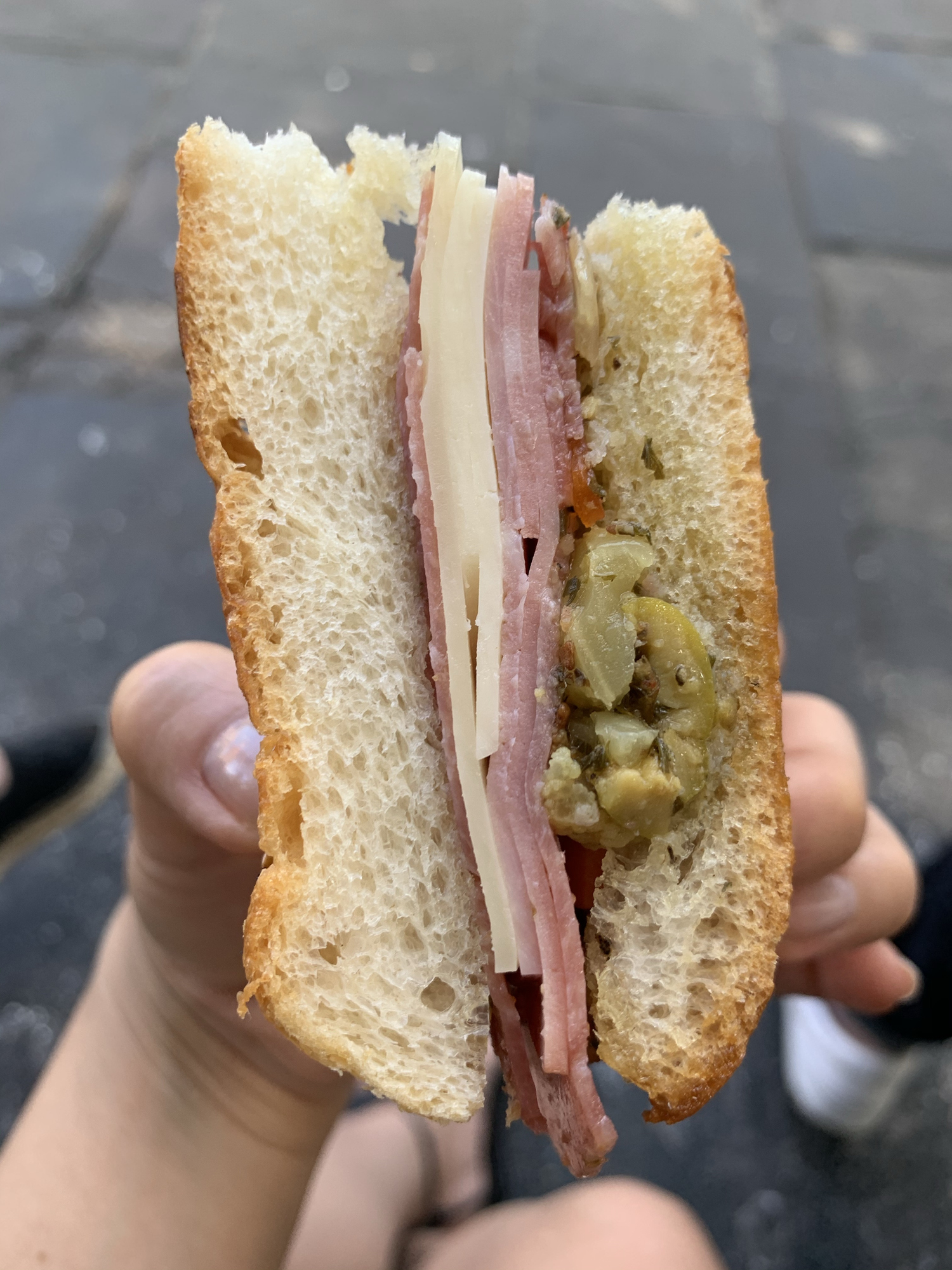 Person holding a sandwich with ham and pickles