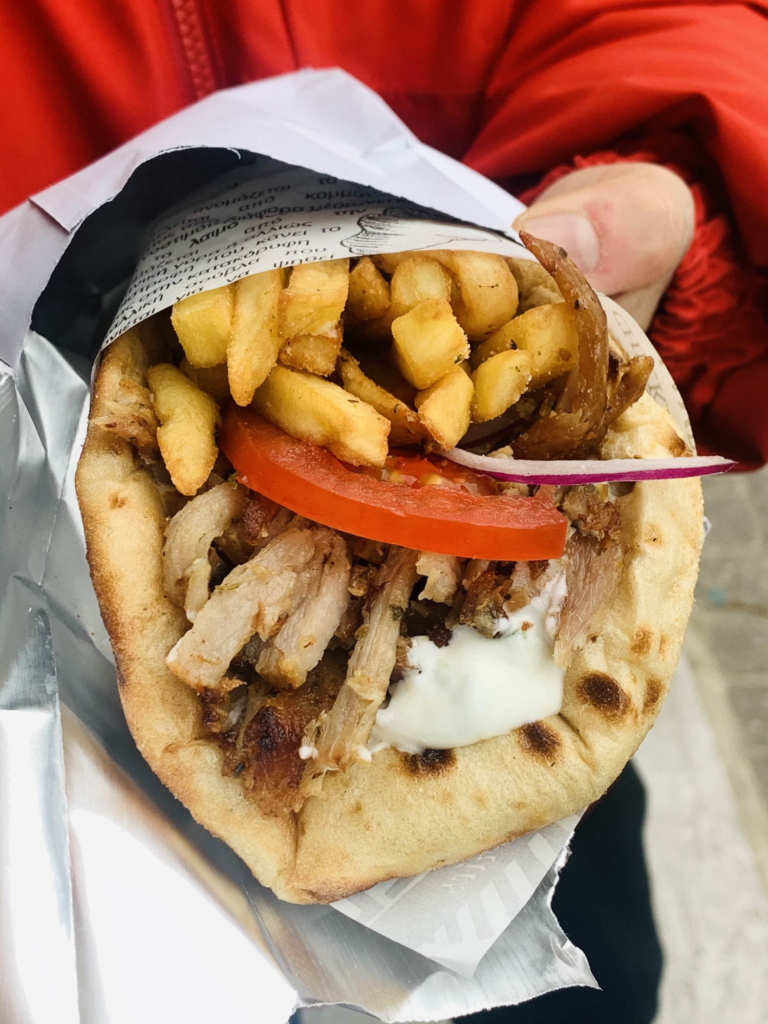 Close-up of a gyro with meat, fries, tomato, and sauce in pita, held in hand