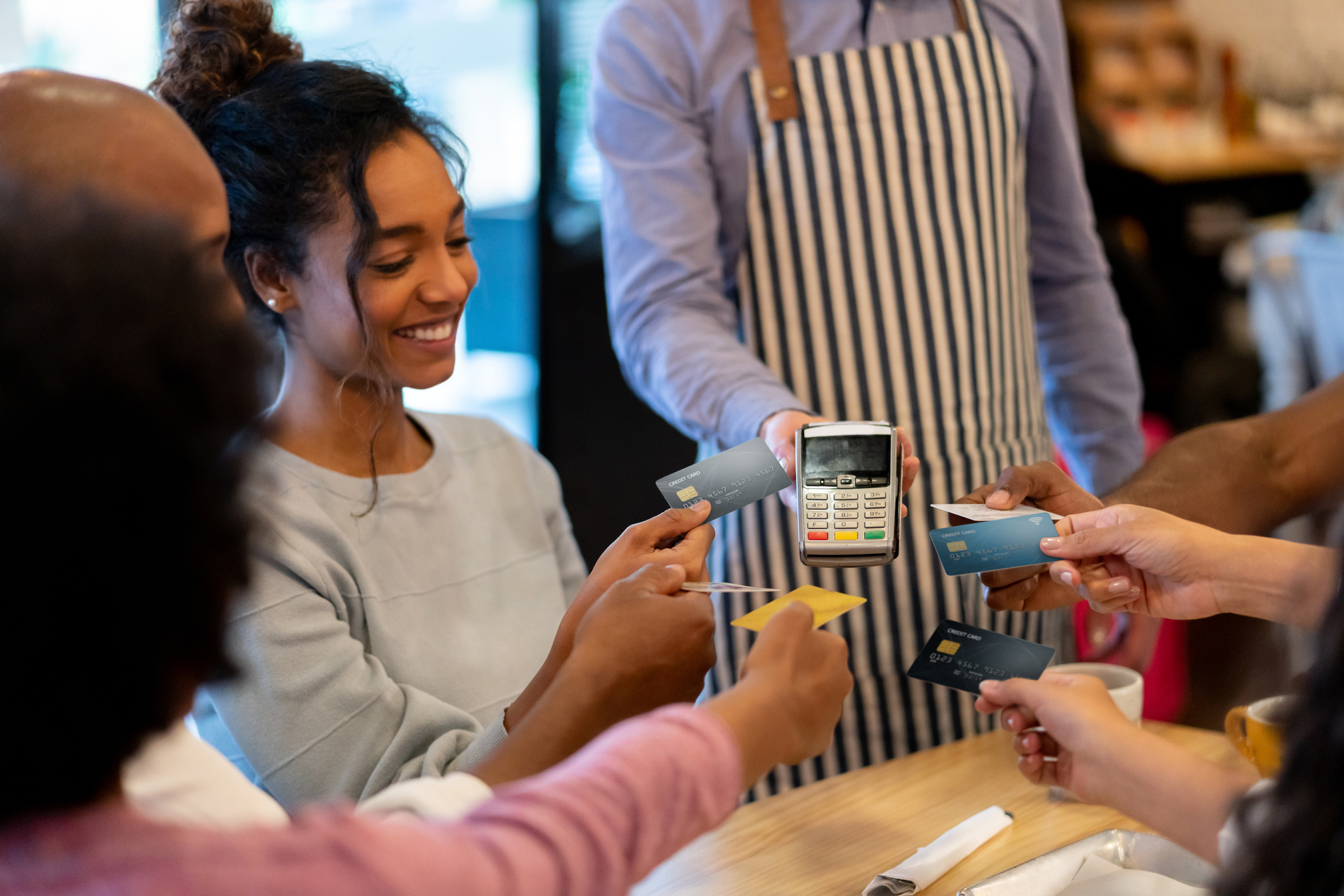 Group of customers handing credit cards to a server holding a card reader