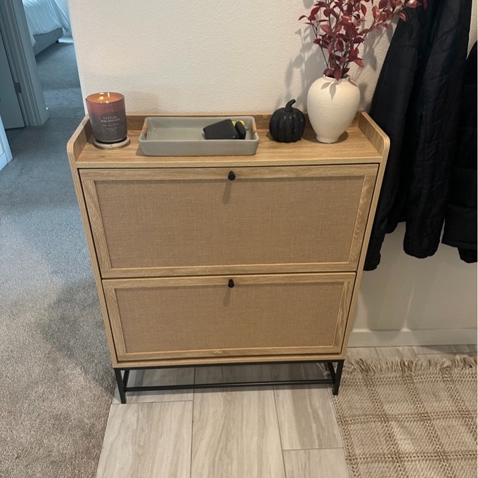 A two-drawer beige fabric-front dresser with a metal frame, topped with a candle, tray, and vase