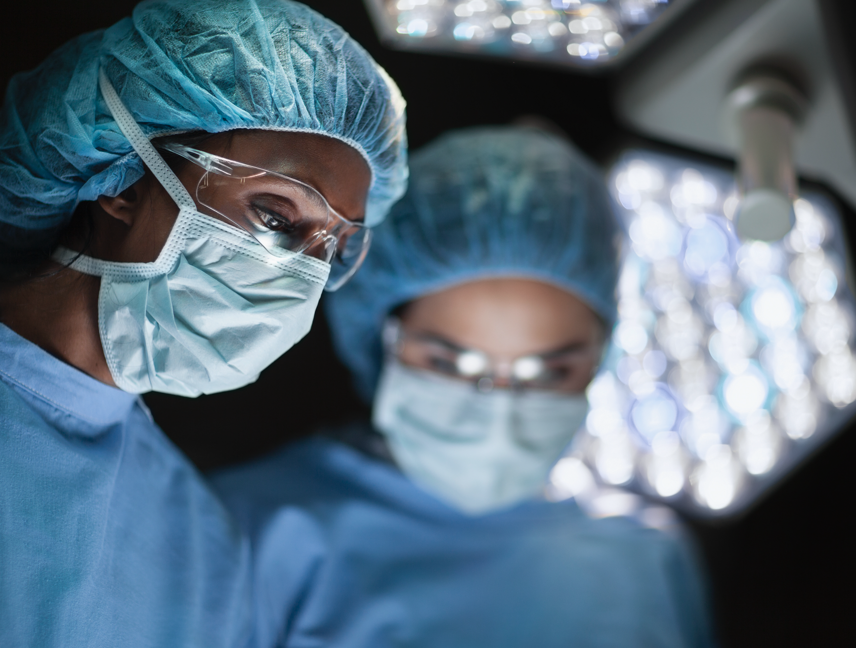 Two surgeons in scrubs and surgical masks focused on a procedure under bright operating lights
