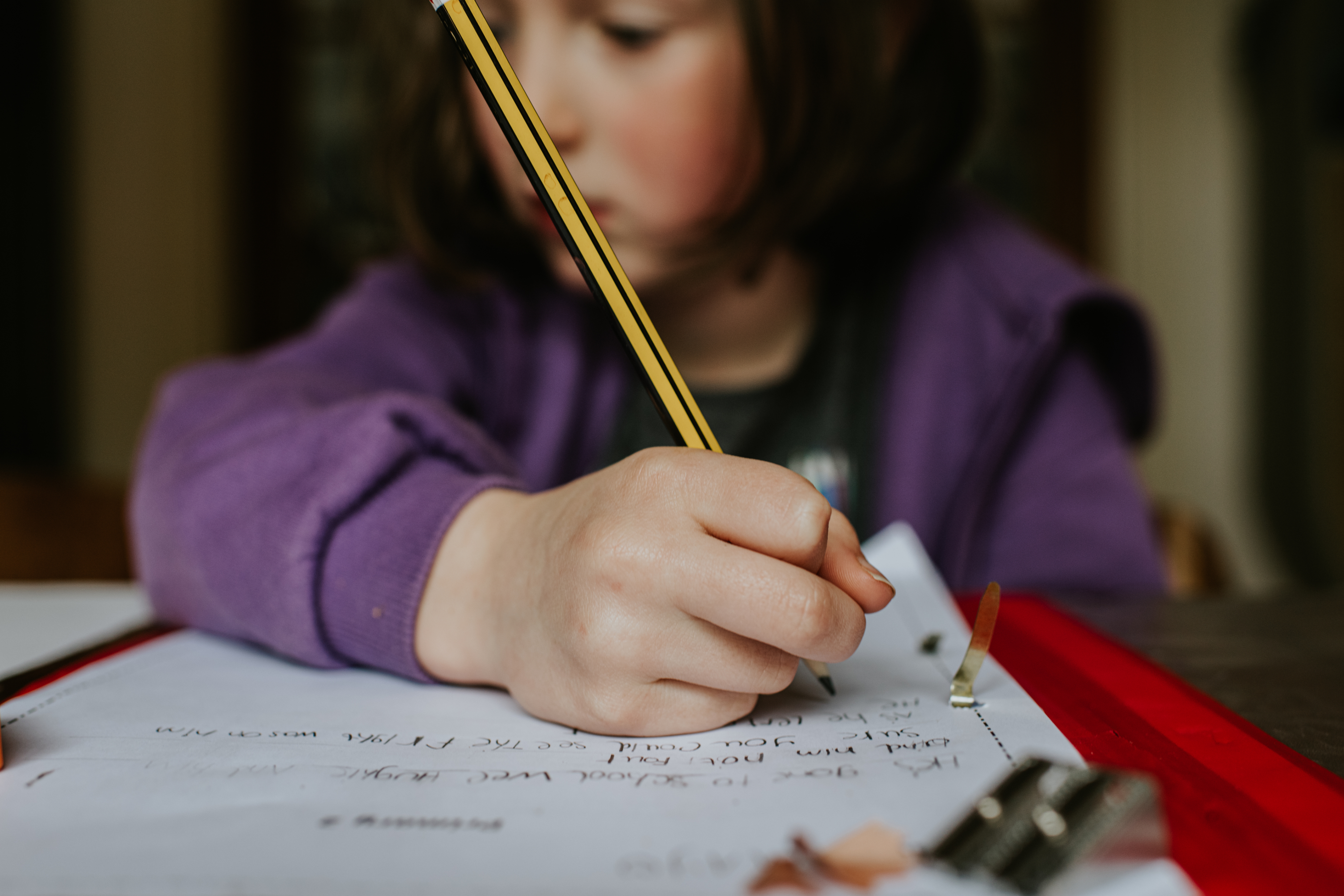 Child focused on writing with a pencil on paper, resting arm on the table