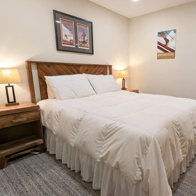 A neatly made bed with a wooden headboard, flanked by two nightstands with lamps. Artwork hangs above the bed