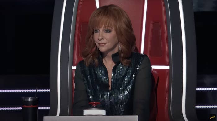 Reba in sparkling top sitting in a judge&#x27;s chair on a talent show set