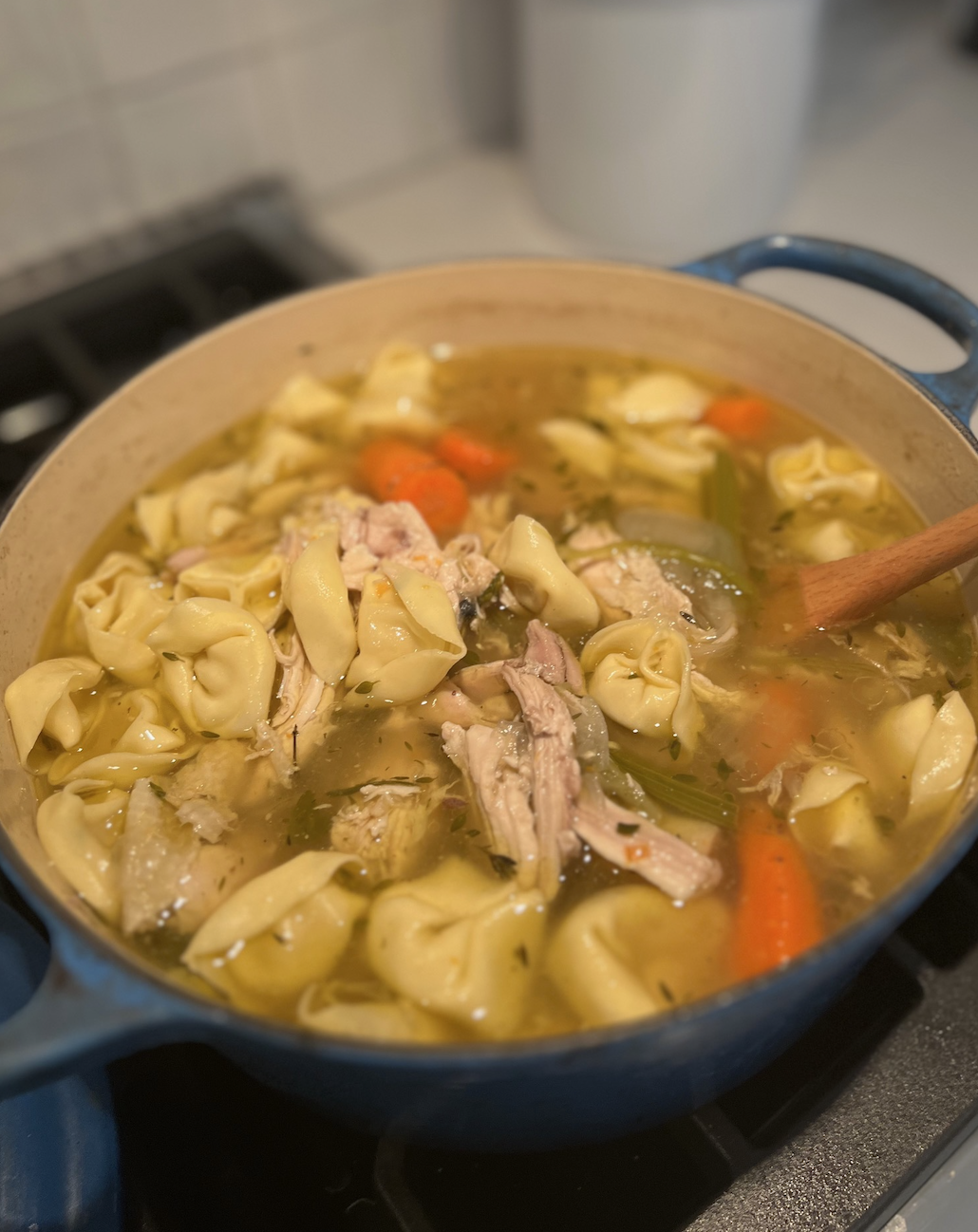 Pot of homemade chicken noodle soup with vegetables and tortellini on the stove