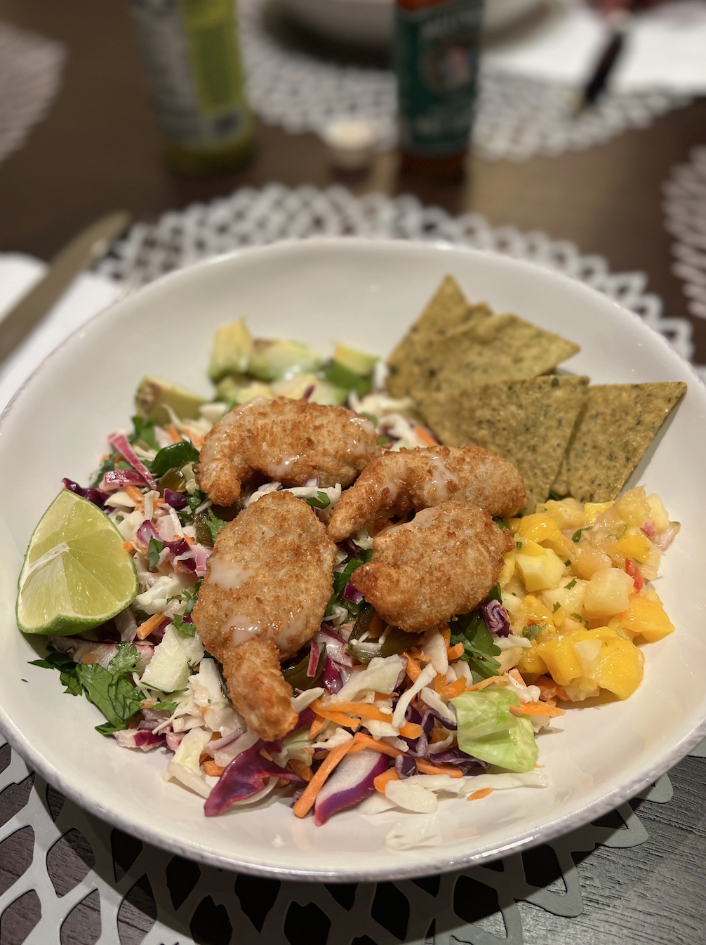 A plate with salad, avocado, lime wedges, shrimp, and tortilla chips on a table