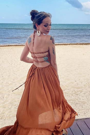 a reviewer in a rust orange backless dress with ruffle tiers, facing the ocean, suitable for beach events