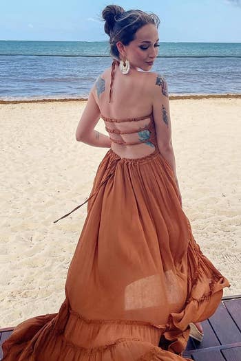 a reviewer in a rust orange backless dress with ruffle tiers, facing the ocean, suitable for beach events