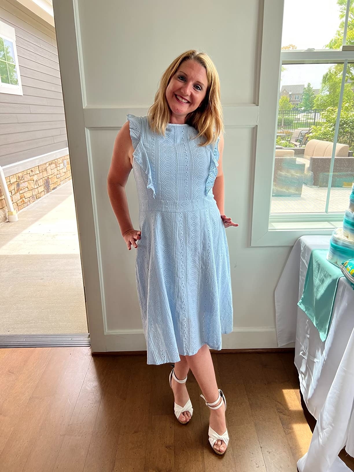 a reviewer in a sleeveless light blue dress with ruffle details, paired with white heeled sandals