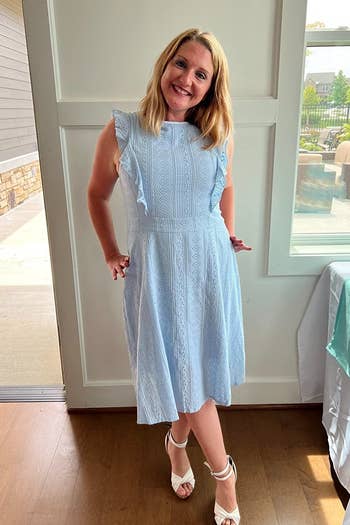 a reviewer in a sleeveless light blue dress with ruffle details, paired with white heeled sandals
