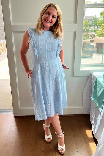 a reviewer in a sleeveless light blue dress with ruffle details, paired with white heeled sandals