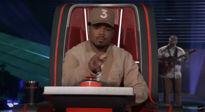 Chance the Rapper in his signature cap and jacket on The Voice, pressing button with artist performing in background