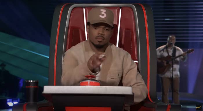 Chance the Rapper in a cap and jacket on The Voice, pressing button with artist performing in background