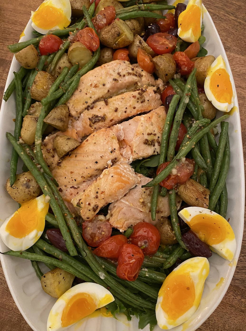 Oval platter of food with salmon, green beans, potatoes, cherry tomatoes, and boiled eggs
