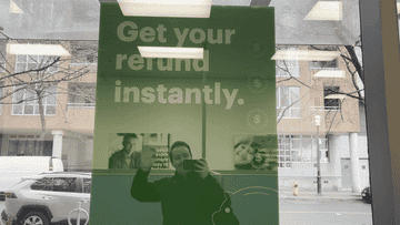 Advertisement for instant tax refunds with obscured reflection of a person taking the photo