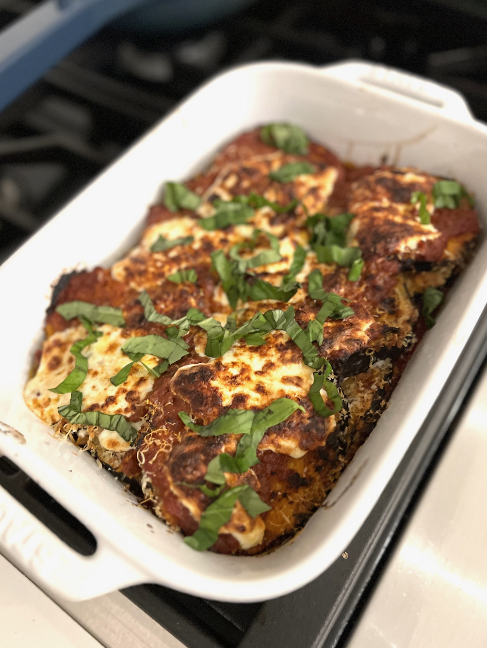A freshly baked lasagna with melted cheese and basil leaves in a white baking dish
