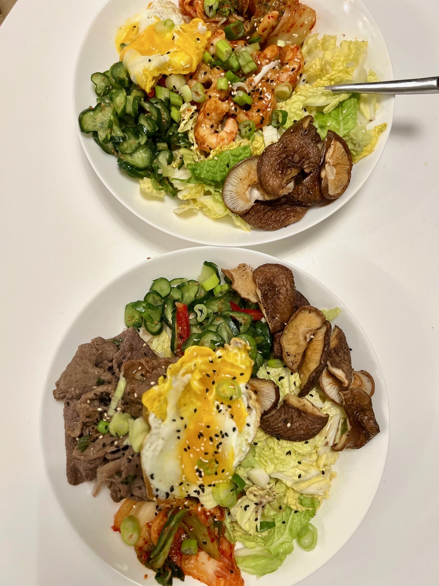Two bowls of salad with assorted toppings including shrimp, beef, mushrooms, and a poached egg