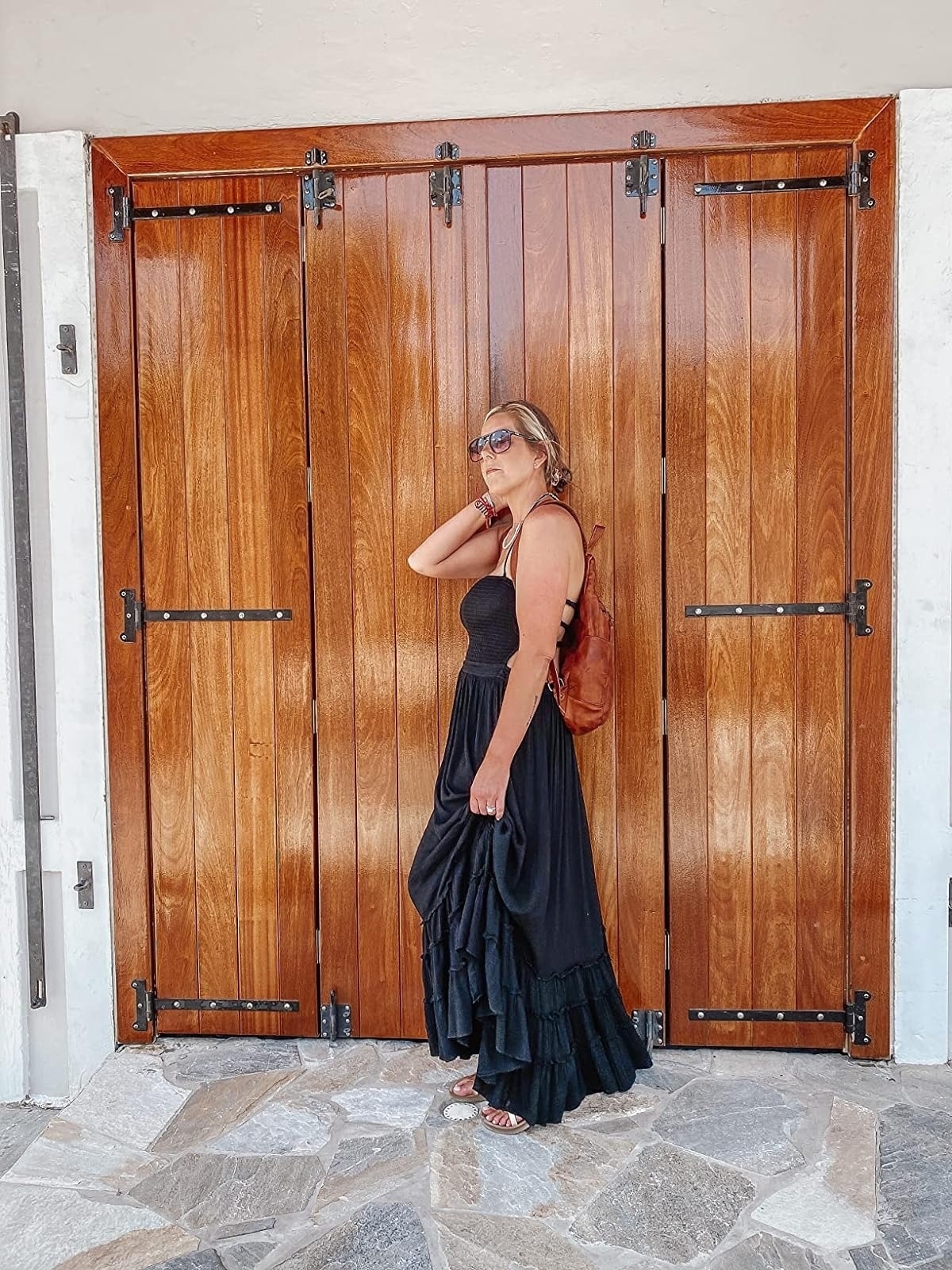 a reviewer in a layered black dress and sunglasses posing against a wooden door