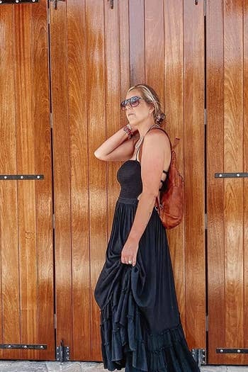 a reviewer in a layered black dress and sunglasses posing against a wooden door
