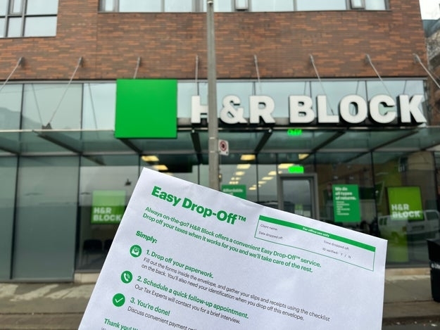 Hand holding H&amp;amp;R Block Easy Drop-Off flyer in front of an H&amp;amp;R Block office