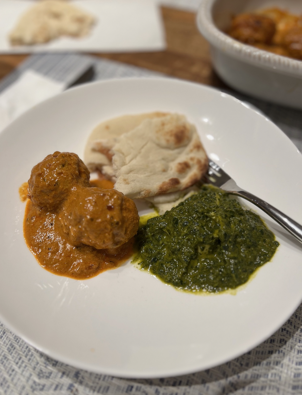 Plate with two meatballs in sauce, a side of spinach, and a piece of flatbread