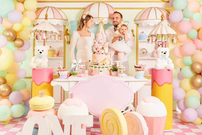Family with a baby at a birthday party with a pastel-themed decoration and a table with sweets and teddy bears
