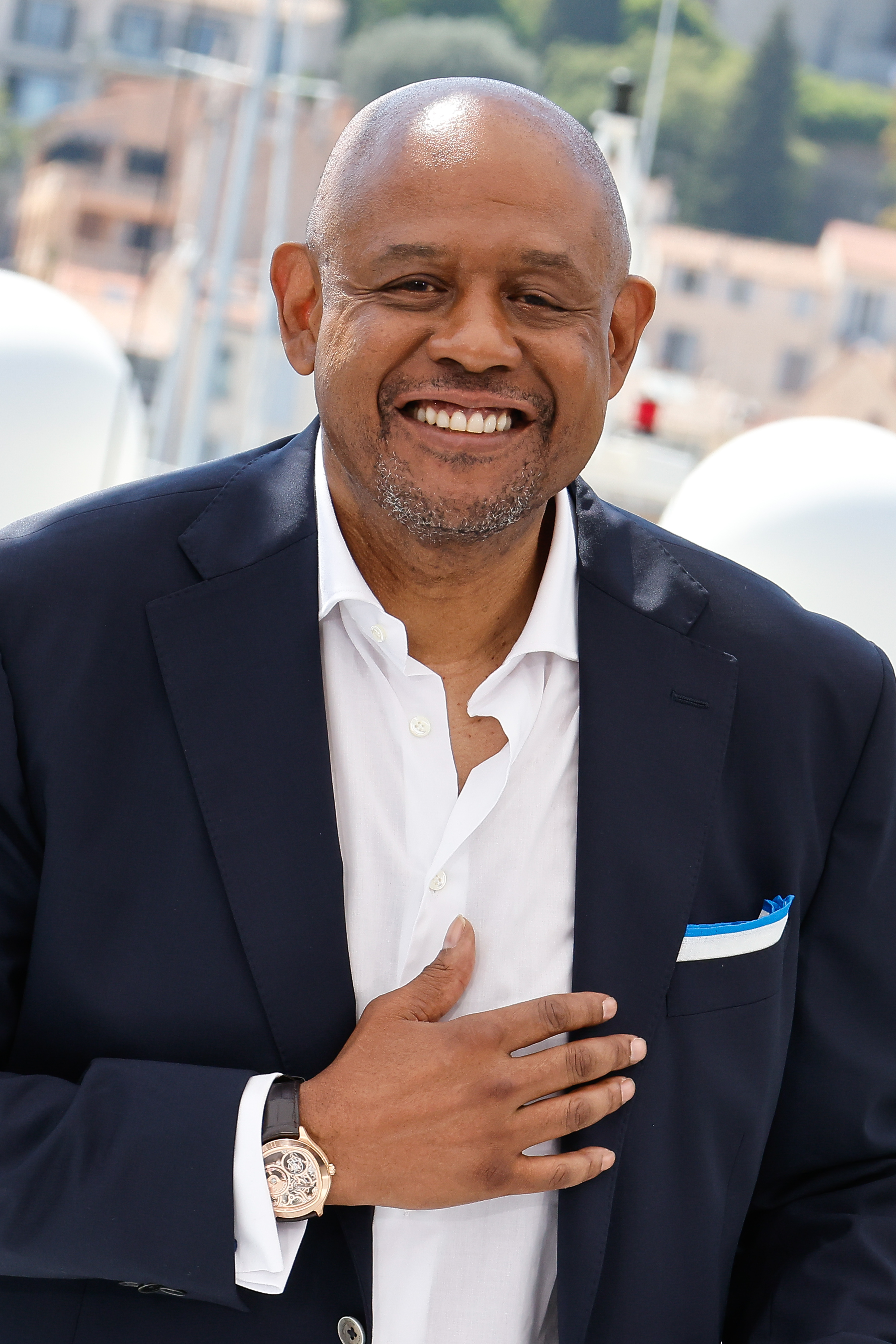 Forest Whitaker wearing a navy suit and white shirt, smiling at an event