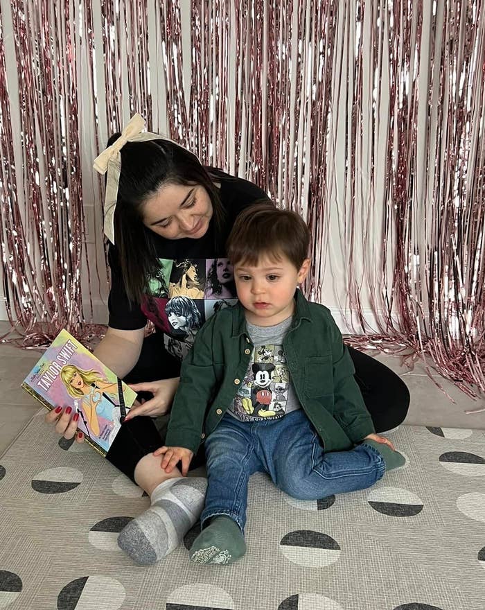 Woman and child sitting on floor reading a book together, with a metallic fringe backdrop