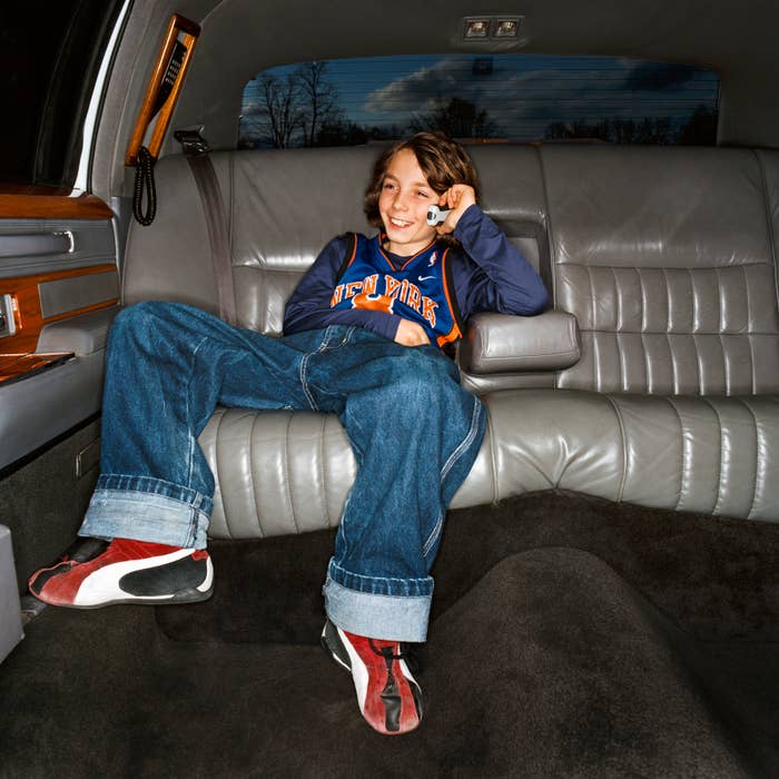 Child in a vehicle, relaxed in blue jeans and sneakers, smiling with one hand behind head