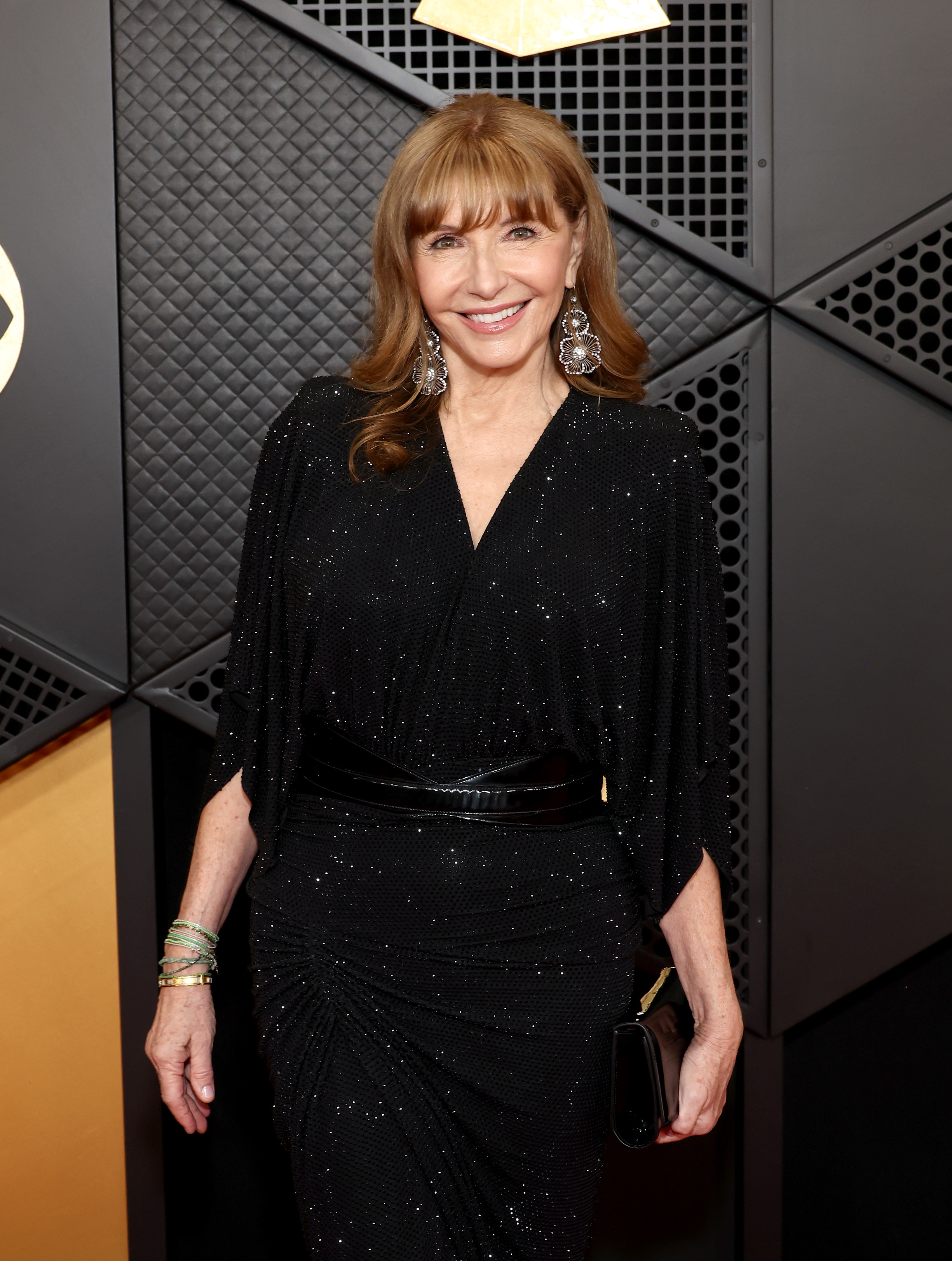 Elegant individual in a sparkling black wrap dress and dangling earrings, posing with a smile