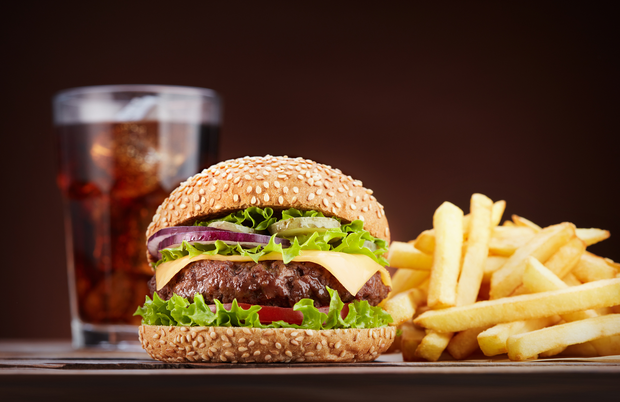 Cheeseburger with lettuce, tomato, and onion, alongside fries and a soft drink