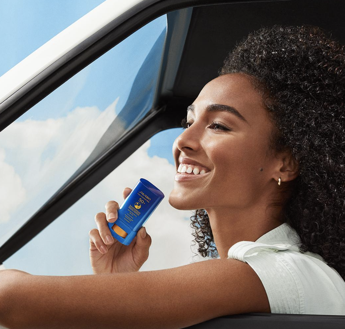Woman in a car smiling at a blue card she&#x27;s holding up to window, implying contactless payment