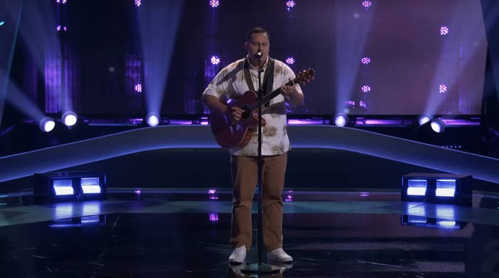 Kamalei playing guitar and singing on stage with spotlights in background