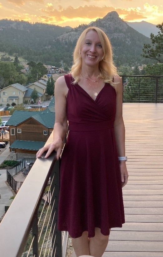 a reviewer in a v-neck burgundy dress standing on a balcony with a mountain landscape in the background